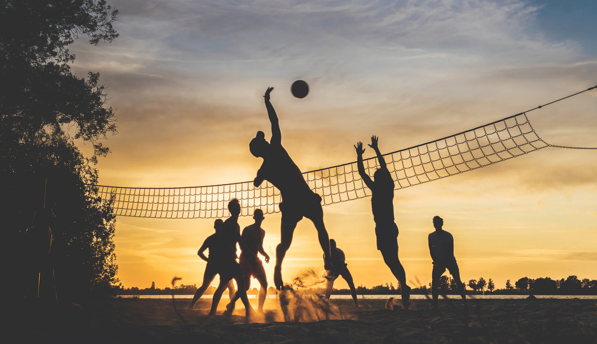 Silhouettes of adults playing beach volleyball at sunset