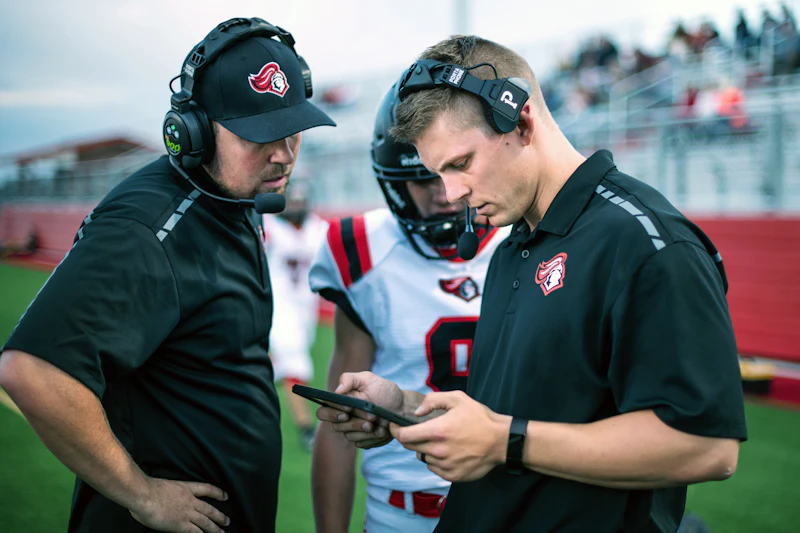 League staff reviewing a game plan on a tablet at the sideline