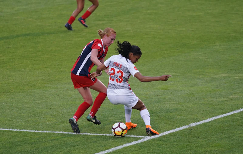 Two adult players battling for the ball in a soccer match